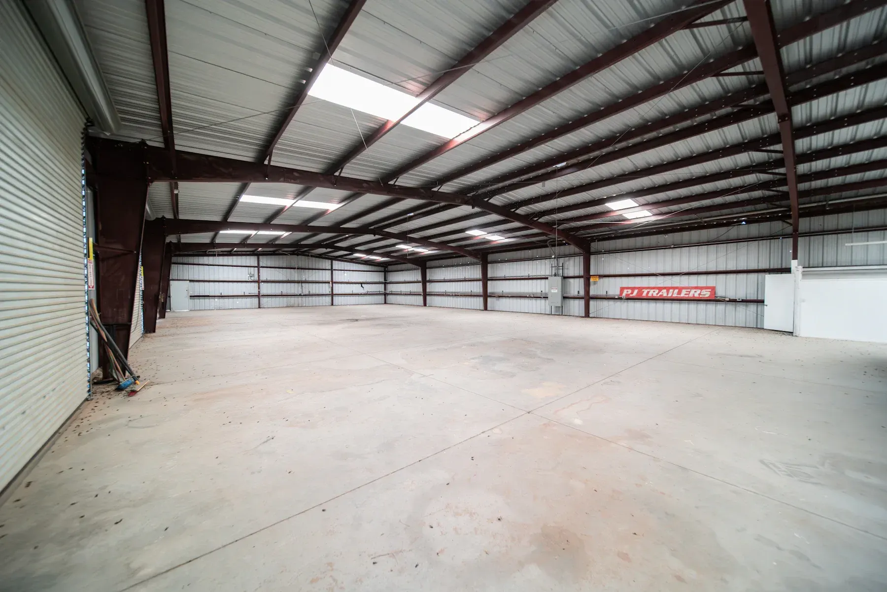 Empty metal-frame warehouse interior with concrete floor and PJ Trailers signage