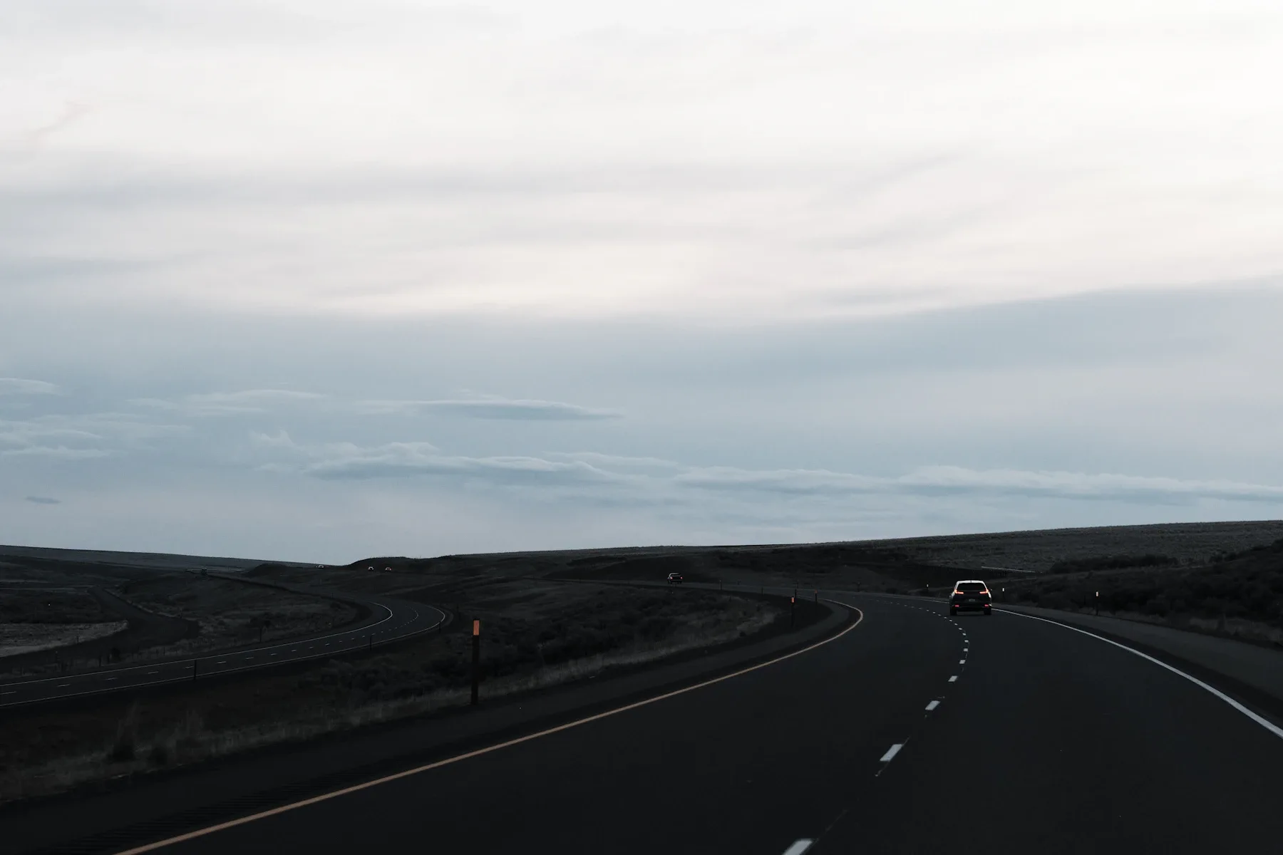 Empty asphalt road curving through dark volcanic landscape with overcast sky
