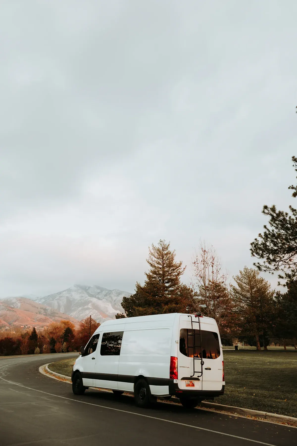 White camper van parked on curved road with mountains and evergreen trees in background
