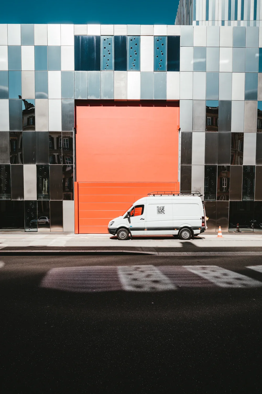 White delivery van parked in front of large orange garage door on checkered building facade