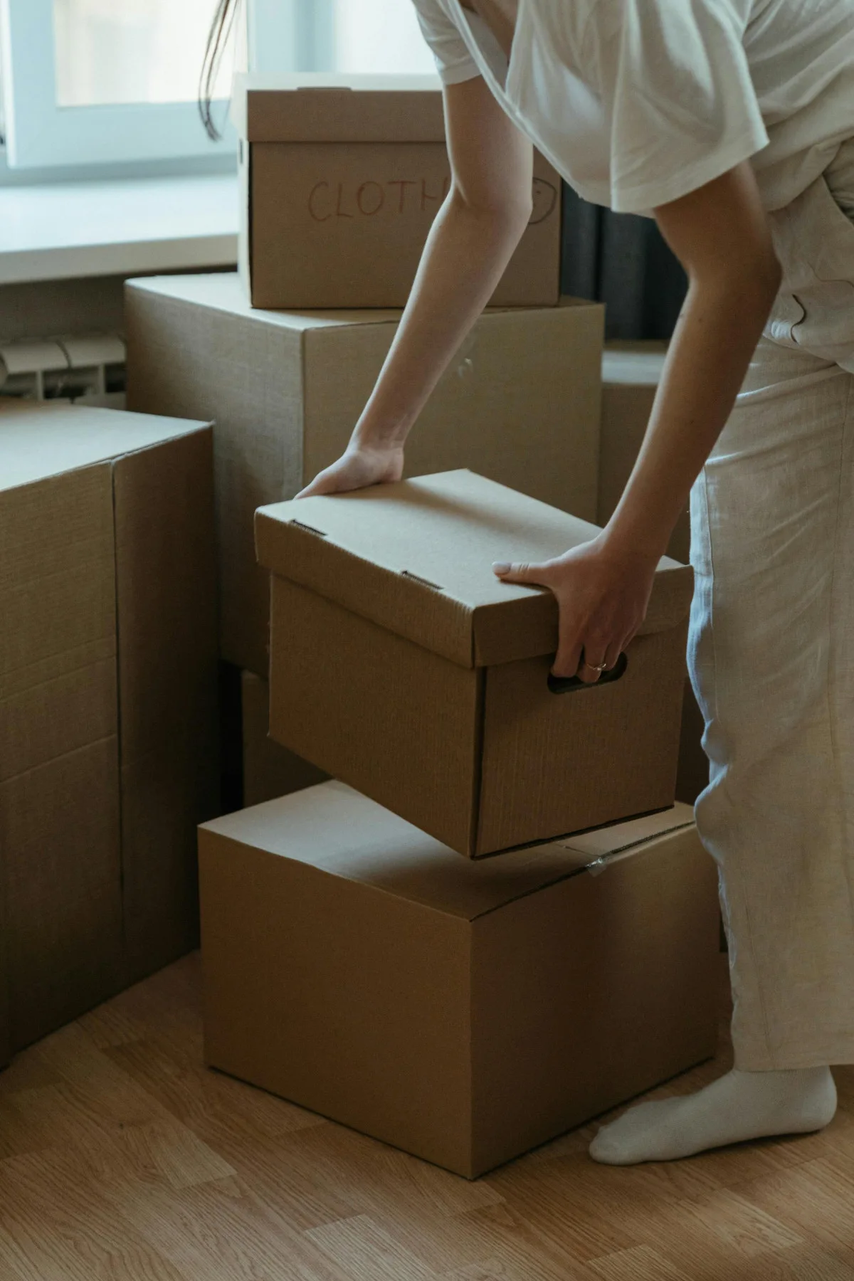 Person organizing stacked cardboard boxes during a move or packing process