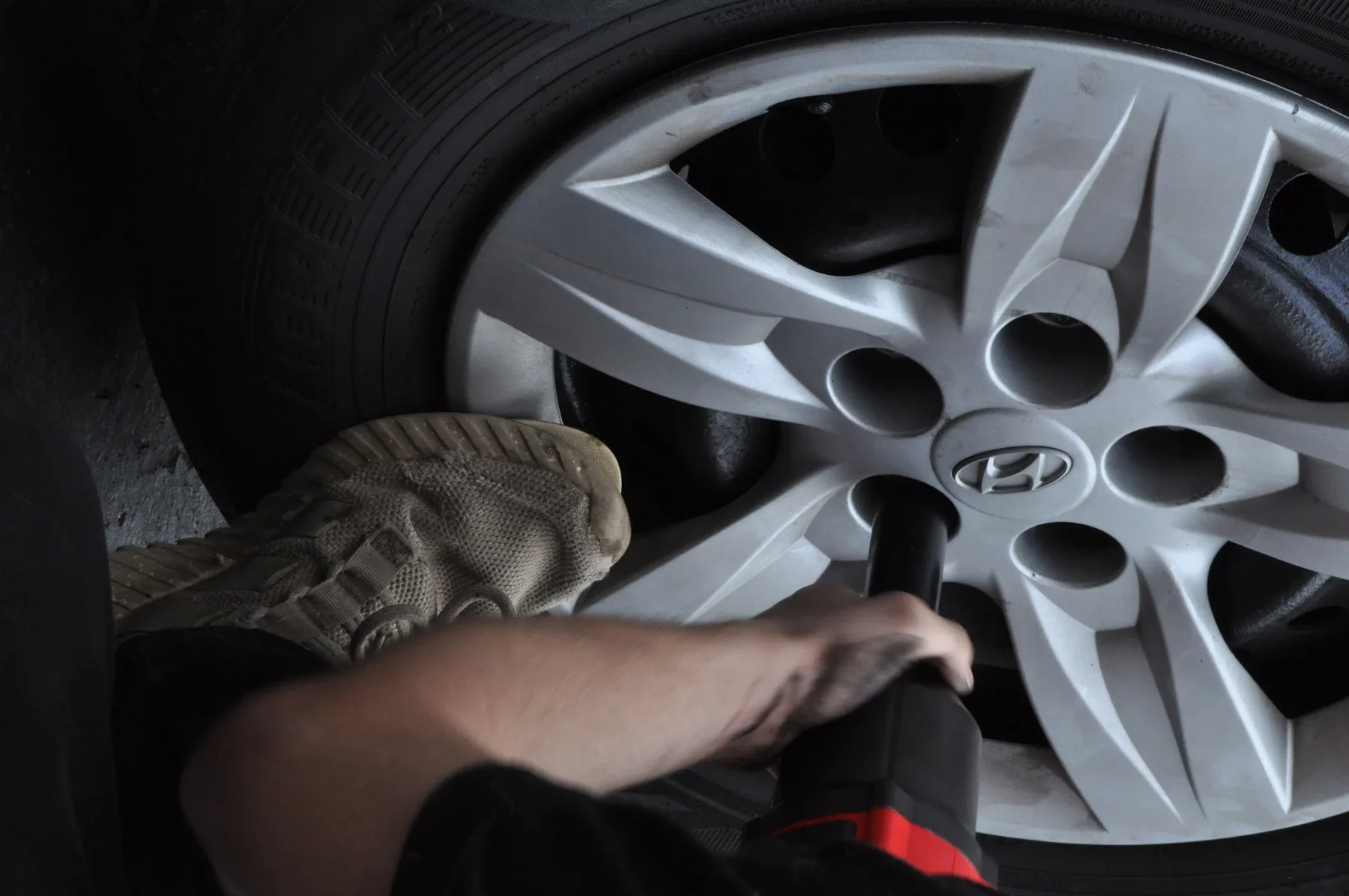 Technician inspecting silver alloy wheel with Hyundai logo on vehicle tire